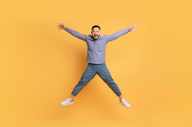 Crazy sales funny asian man jumping like a star over yellow background