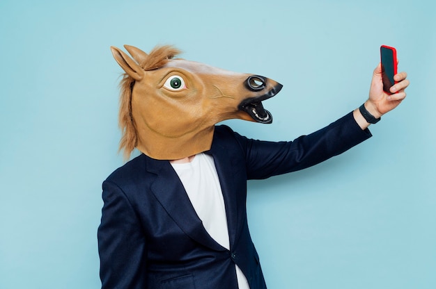 Photo crazy senior man wearing horse mask and taking selfie with mobile smartphone