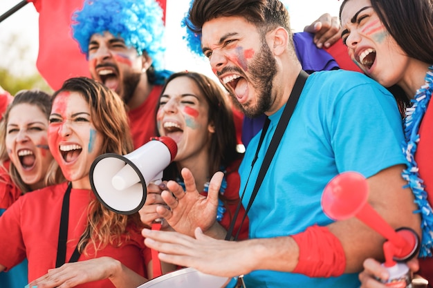 Foto appassionati di sport pazzi che suonano la batteria e urlano mentre sostengono la loro squadra di calcio - obiettivo principale sul volto di un giovane uomo