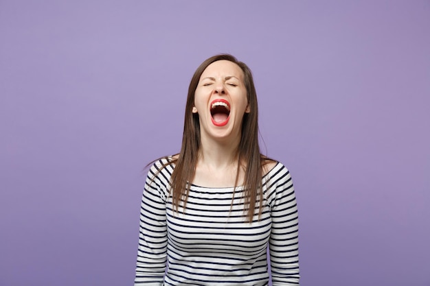 Crazy wild young brunette woman in casual striped clothes posing isolated on violet purple background studio portrait. People lifestyle concept. Mock up copy space. Keeping eyes closed, screaming.