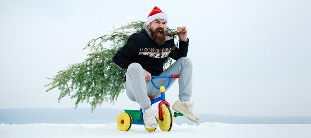 Uomo pazzo di inverno sulla bicicletta che si prende cura dell'albero di natale uomo con pupazzo di neve sulla neve di sfondo invernale all'aperto