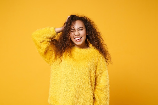 Photo crazy young african american girl in fur sweater posing isolated on yellow orange wall background studio portrait. people lifestyle concept. mock up copy space. putting hand on head, showing thumb.