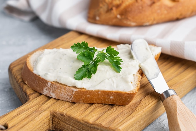 Foto crema di formaggio alle erbe e condimento su fetta di pane fresco di segale croccante con coltello da formaggio nelle vicinanze