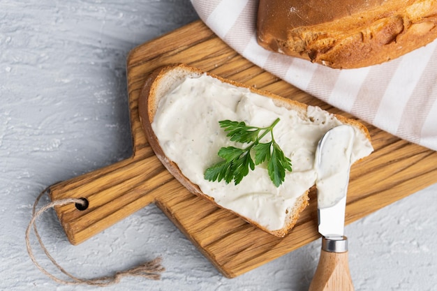 Photo cream cheese with herbs and seasoning on slice of fresh crunchy rye bread with cheese knife nearby