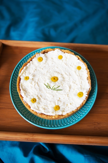 A cream cheesecake stands on a wooden tray in bed. view from above.