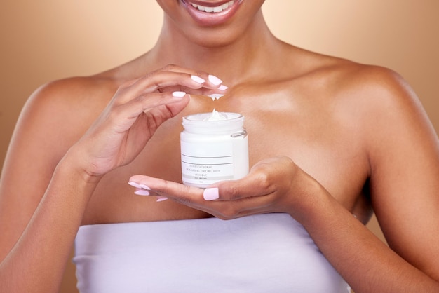 Cream container and woman hands for skincare beauty and cosmetics application on brown background Happy person or skin care model with body lotion or moisturizer for dermatology health in studio