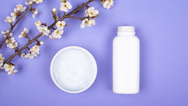 Cream cosmetics and flowering twigs on violet background. skin care concept, beauty.