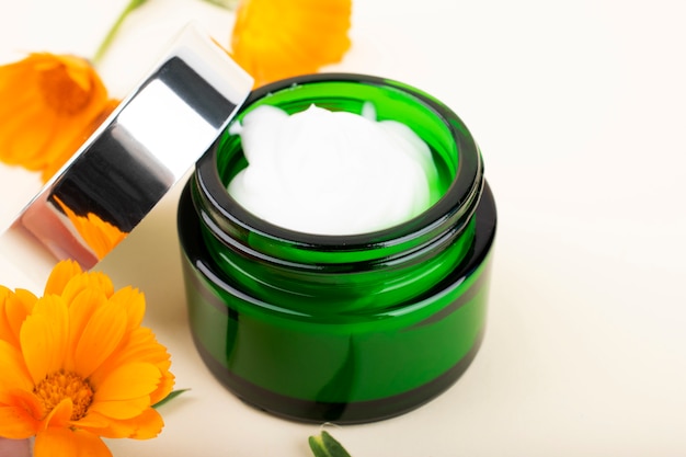 Cream for face and body. Green jar with calendula cream and orange flowers.