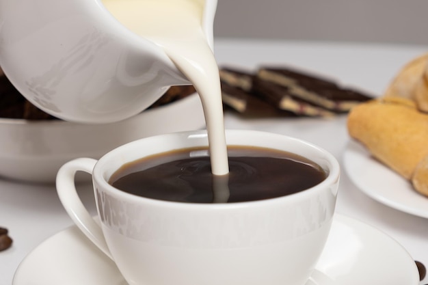 Cream from the milk jug is poured into coffee making coffee with cream cappuccino