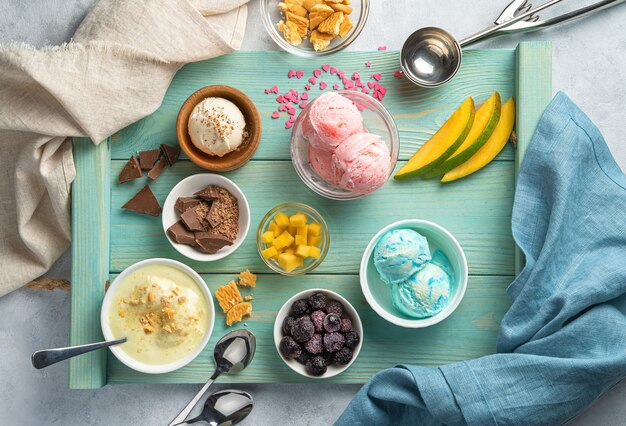 Cream ice cream of different types, fruits and frozen berries on a light blue wall. Top view, horizontal.