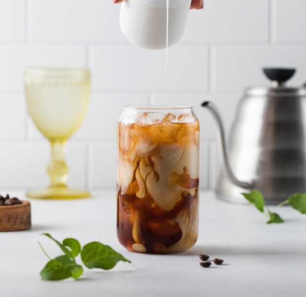 Cream is poured into cold black coffee with ice cubes coldbrew summer drinks