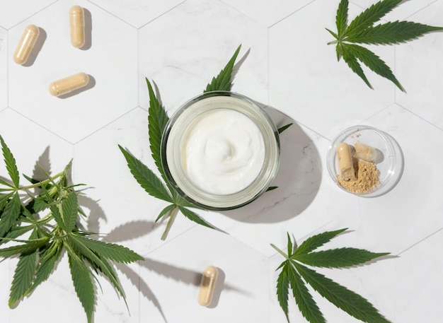 Photo cream jar and capsules with hemp protein powder near green cannabis leaves