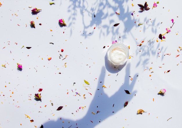 Cream jar and dry flowers on white surface. Above view