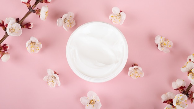 Cream jar and flowers on pink surface