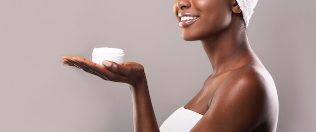 Cream jar on open palm of smiling african american woman