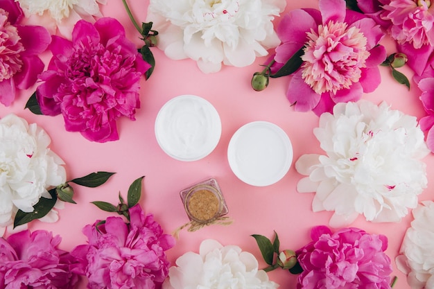 A cream mask and bottle sea salt on a light pink background with a delicate peony flower Mock up image