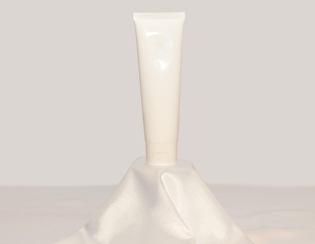 白い絹の生地の表彰台にクリーム色のモックアップ優しいスキンケアのコンセプト