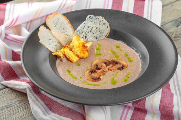 Cream of mushroom soup in dark bowl. Homemade creamy soupe with sliced boletus mushrooms.