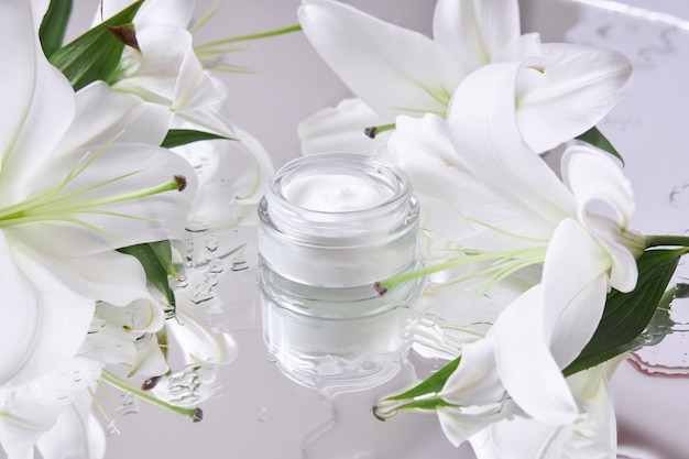 Cream for skin care, natural cosmetics made of flowers and petals. A glass jar of white cream stands among the lily flowers