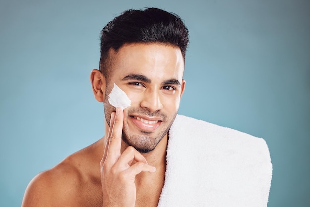 Cream skincare and portrait of the face of a man with moisturizer after a shower against a blue mockup studio background Sunscreen wellness and smile of a young model with facial creme for skin