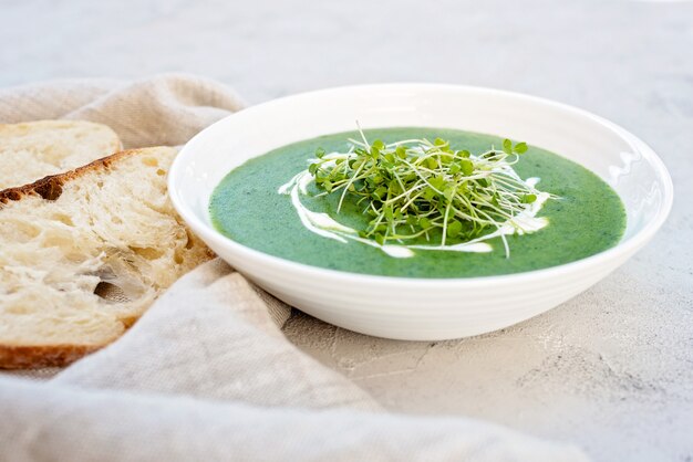 Cream soup of fresh spinach with arugula microgreen in a white plate with ciabatta bread