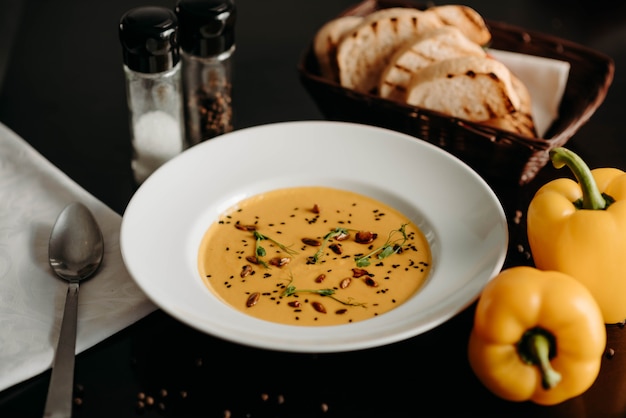 Cream soup on a served table with yellow pepper and slices of bread