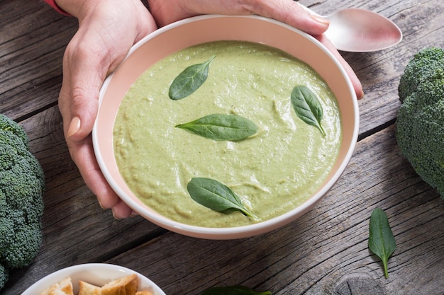 Крем-суп с брокколи и шпинатом в женской руке Чаша с гренками
