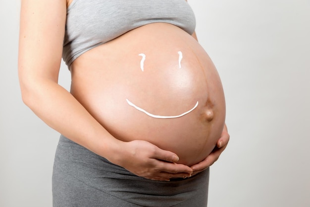 Cream on the stomach of a pregnant girl in the form of a smiley Skin care prevention of stretch marks