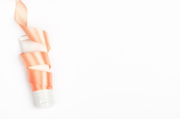 Cream tube wrapped in ribbon on white background.