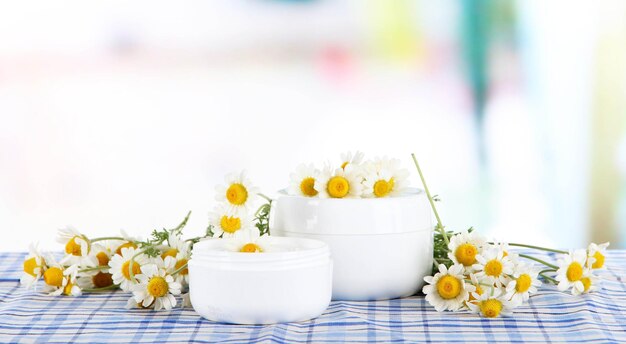 Cream with chamomile on checkered cloth on room background