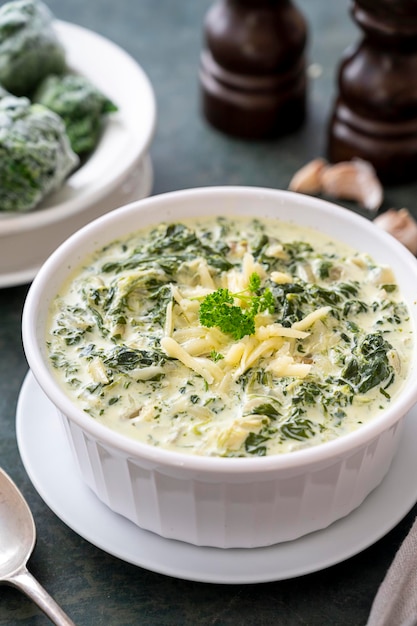 Creamed spinach with cheese in white bowl on dark background Healthy foods