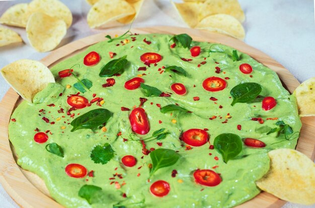 Creamy avocado board with chili peppers herbs and nachos Selective focus with blurred foreground and background