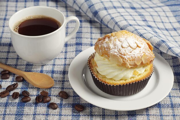 Creamy cake and cup of hot coffee on table covert blue tablecloth