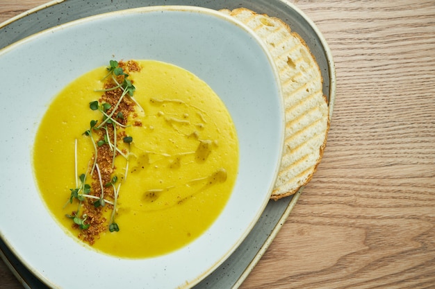 Creamy cream soup in a beautiful bowl with crackers, fried bread and microgreen. Tasty food for lunch. wooden background