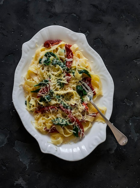 Creamy fettuccine pasta with dried tomatoes and spinach on a dark background top view