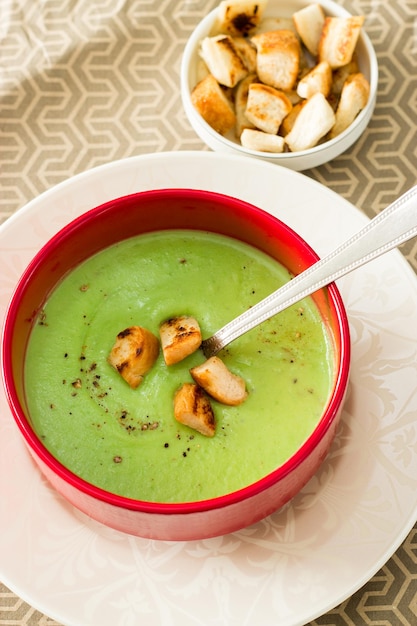Фото Сливочный суп из зеленого горошка с гренками в красной миске вид сверху диетическое питание