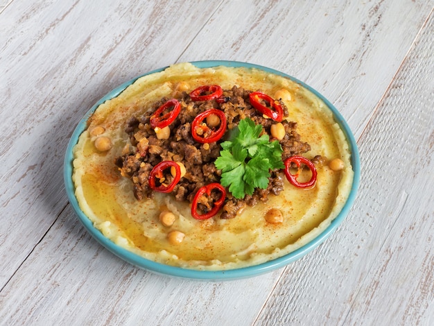 Creamy hummus with spicy mutton minced meat on a white wooden background. Ramadan food.