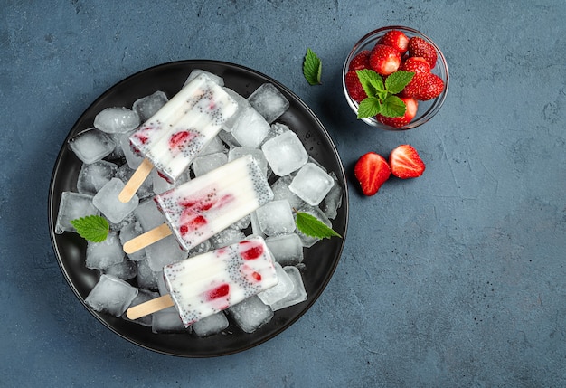 Creamy ice cream with berries and chia seeds on a black plate with ice on a dark blue background