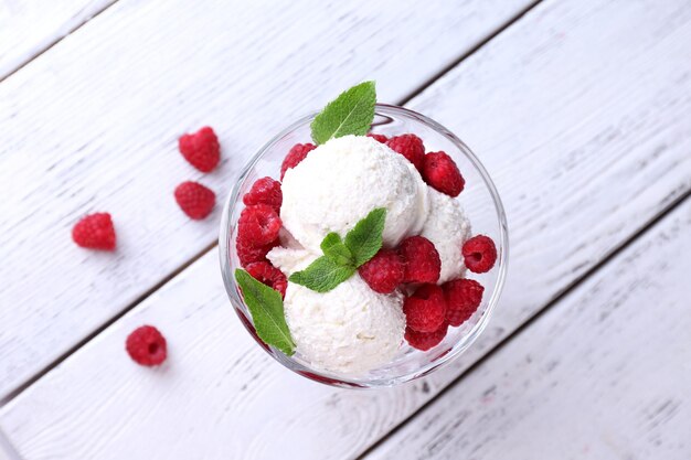 Creamy ice cream with raspberries on plate in glass bowl on color wooden background