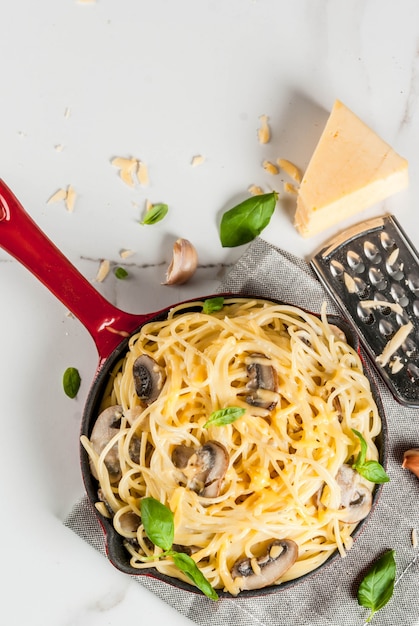 Creamy mushroom pasta with cheese and basil, in portioned frying pan, on white marble table top view