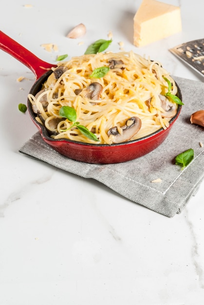 Creamy mushroom pasta with cheese and basil, in portioned frying pan, on white marble table, 