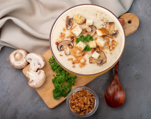 Photo creamy mushroom soup with cream with white bread croutons in a yellow bowl on a gray textured background. view from above.