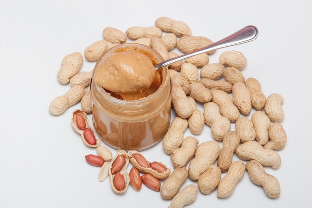 Creamy peanut butter in glass jar peanut and spoon isolated on white background A traditional product of American cuisine