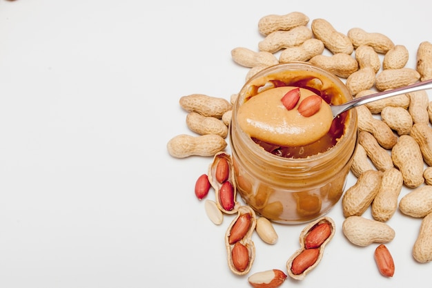 Creamy peanut butter in glass jar, peanut and spoon isolated on white