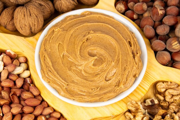 Creamy peanut butter peanut butter in an open glass jar in the center of a peanut food background Peanuts in shell peeled peanuts on a white background Vegan food concept Creamy peanut butter flat