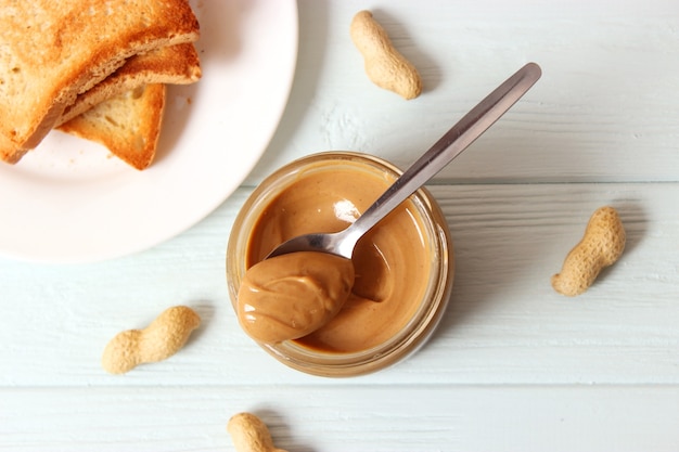 Creamy peanut butter and peanuts beans on wooden background top view. High quality photo