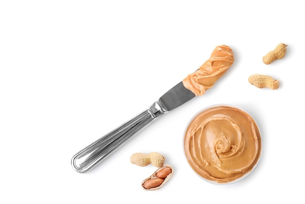 Creamy peanut butter in small bowl and knife with peanut butter isolated on white