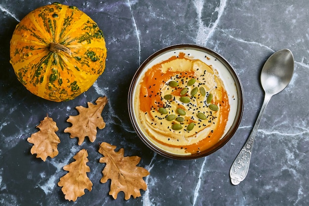 Creamy pumpkin soup with cream and seeds in a bowl against a dark marble table