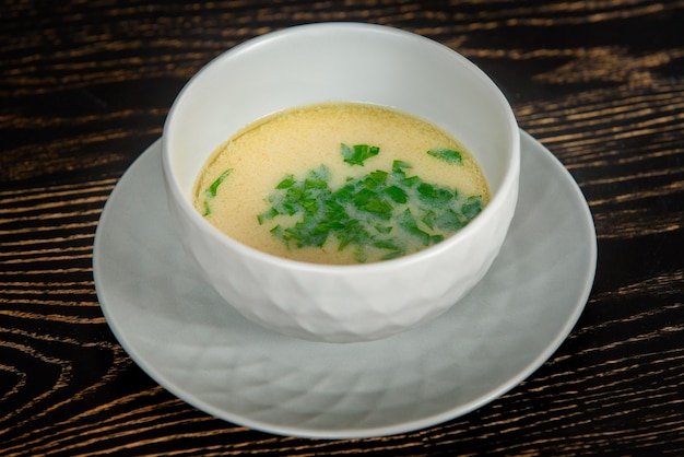 暗い木製のテーブルの上の皿の上の灰色のボウルにハーブで飾られたクリーミーなスープ。
