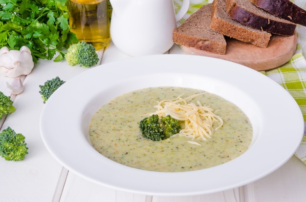 Creamy soup puree with broccoli, green peas, cheese and fresh herbs in a white plate 